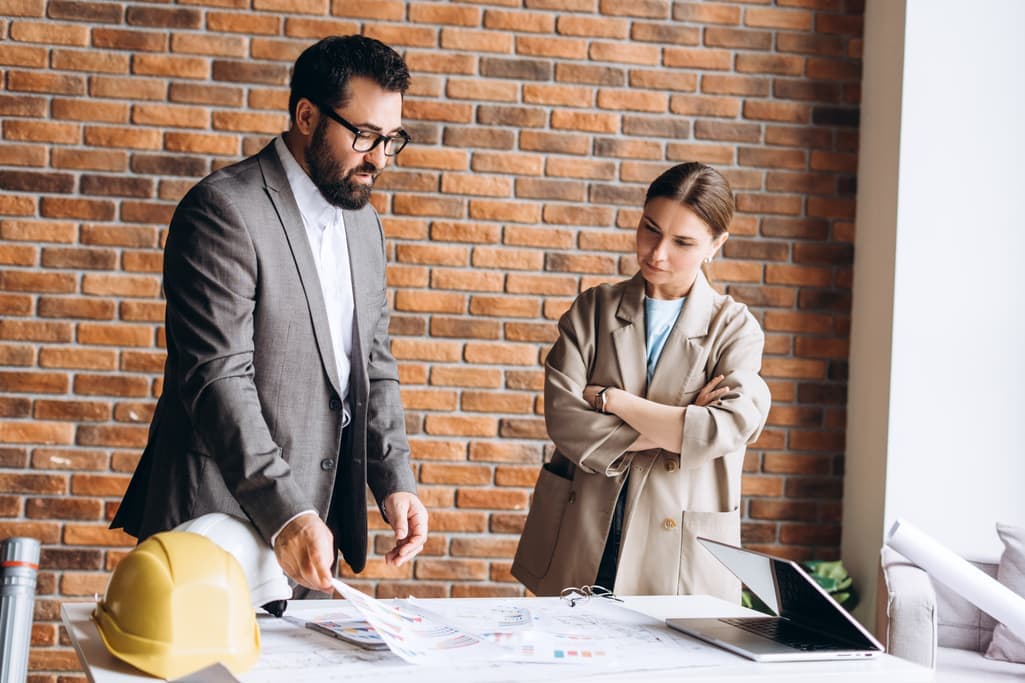 Two architects reviewing drawings at a desk by a brick wall