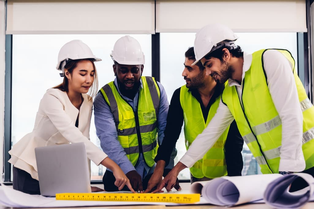 Engineers in hard hats and high-vis vests reviewing plans on a laptop
