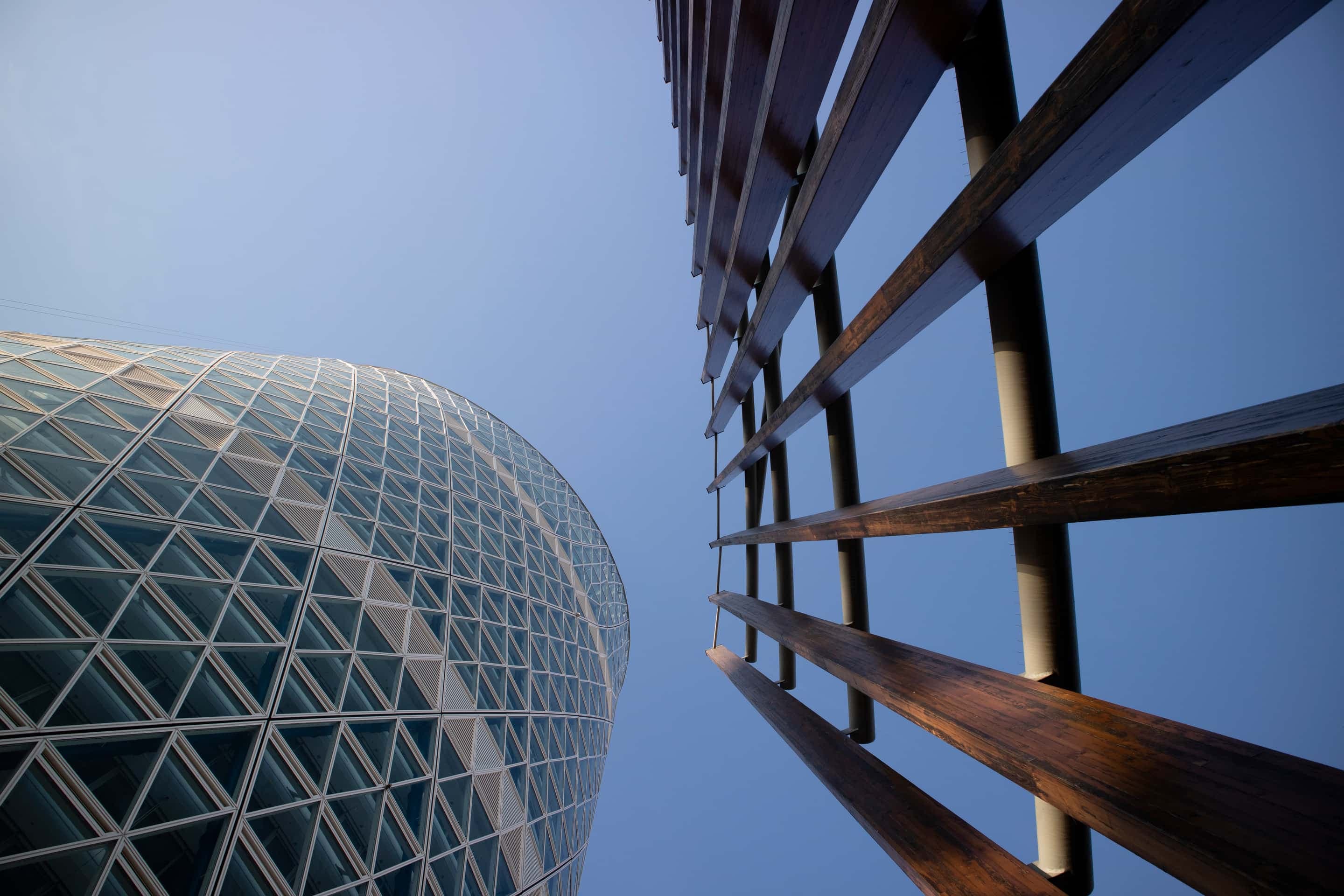 Looking up at a curved glass-grid tower beside timber fins