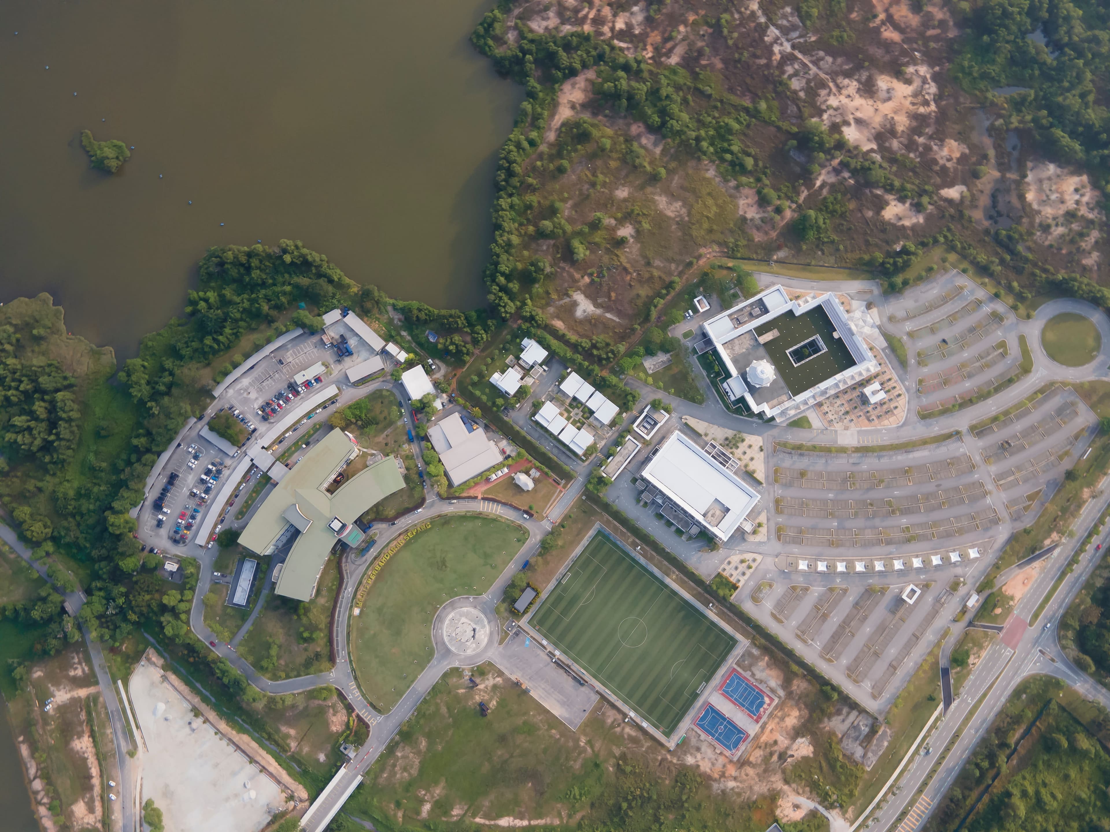 Aerial rendering of a lakeside campus with sports fields and parking